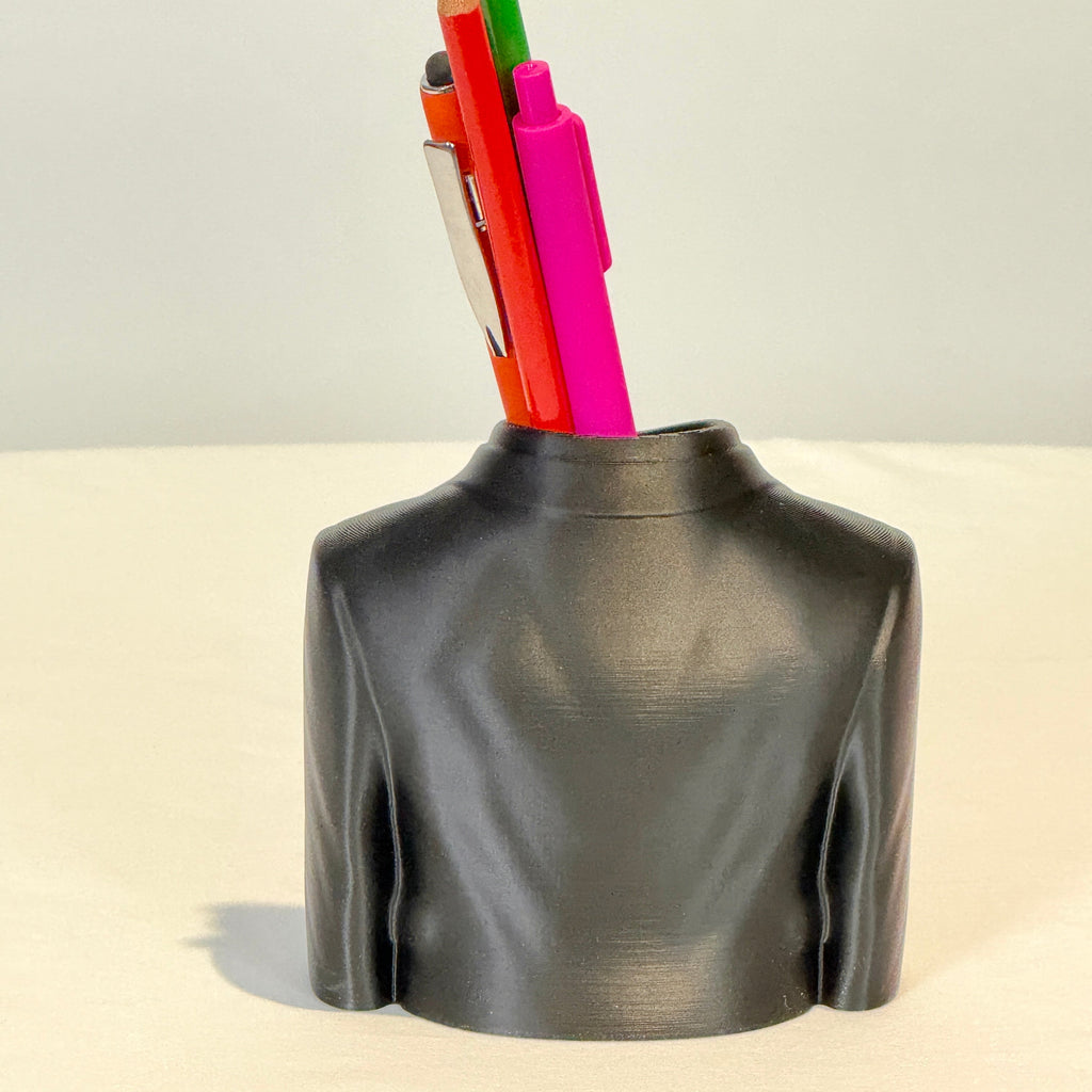 Black leather-textured vase holding colorful pens and pencils on a beige background