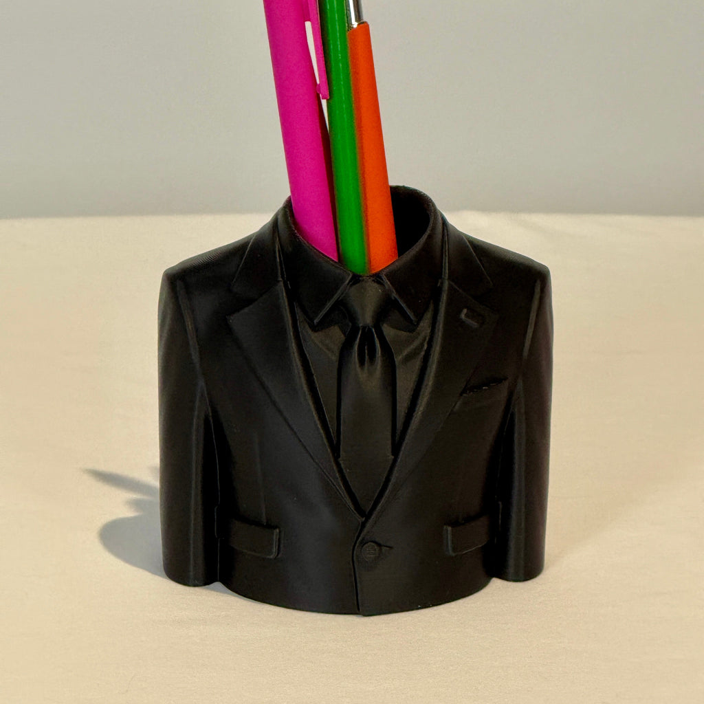 Black suit-shaped pen holder with colorful pens on a beige surface