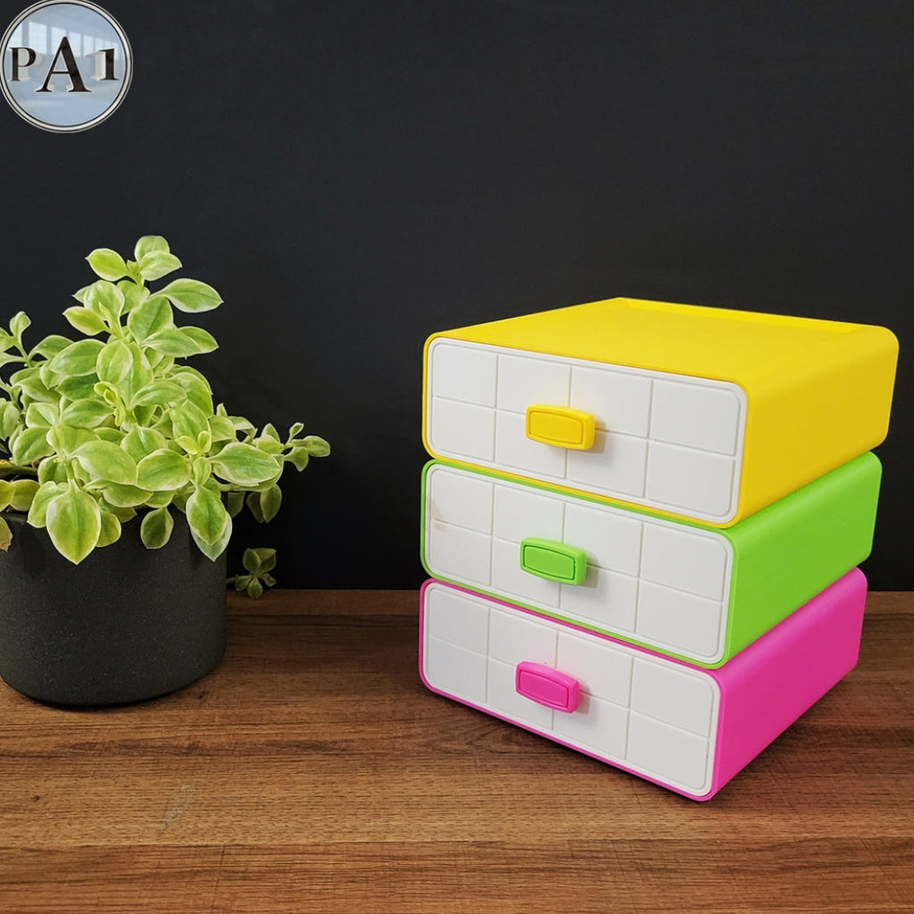 Stack of colorful plastic drawers on a wooden surface with a plant in the background