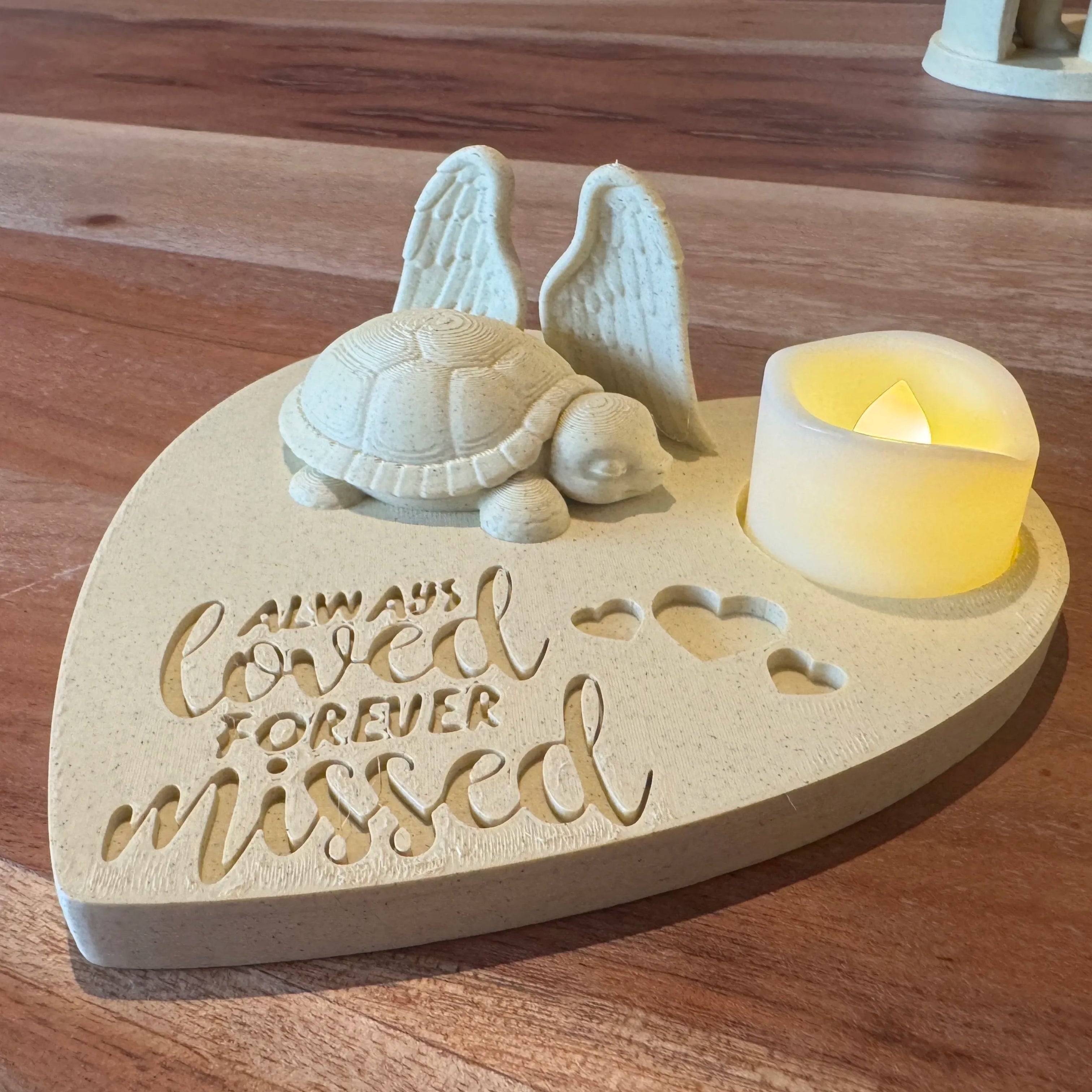 Heart-shaped wooden plaque featuring a turtle with Angel wings figurine and LED candle on a wooden surface.